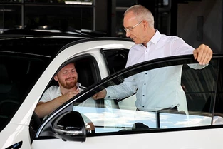 Verkäufer von Mercedes-Benz übergibt Kunden der im Auto sitzt den Fahrzeugschlüssel
