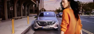 Mercedes-Benz EQC im Hintergrund mit orange gekleideter Frau im Vordergrund