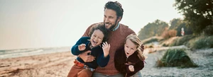 glücklicher Mann am Strand mit zwei Kindern im Arm