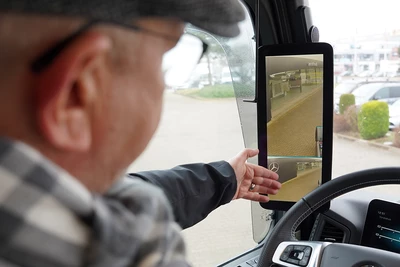 LKW Fahrer schaut in den Spiegel und auf Display der Rückfahrkamera