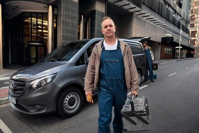 Mann mit Werkzeugkoffer steht vor grauem Mercedes-Benz Vito