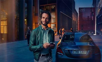 Mann steht mit Handy in der Hand vor silbernem Mercedes