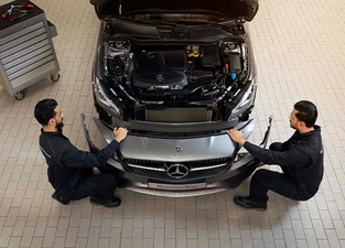 Zwei Monteure arbeiten an silbernem Mercedes