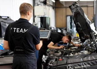 zwei Kfz Mechaniker arbeiten an einem Auto in der Werkstatt